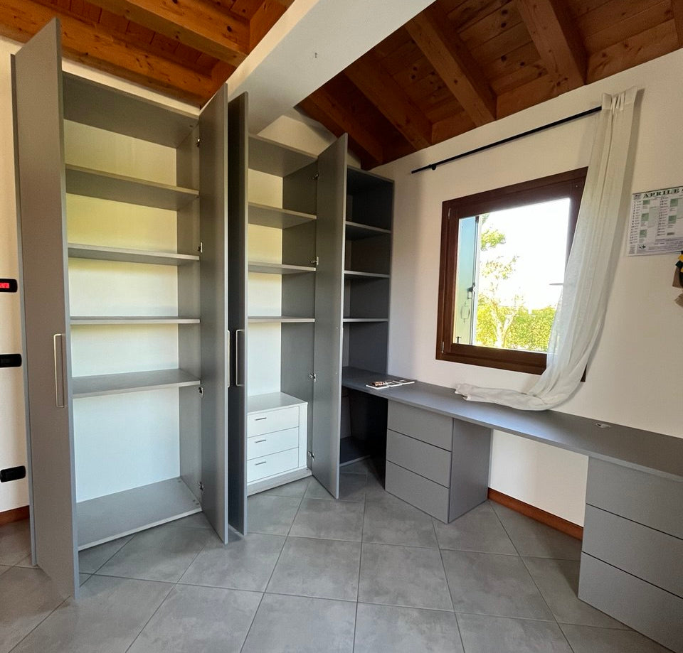 un armadio con ripiani, un armadio con cassettiera intera, una libreria e infine una scrivania sostenuta da due cassettiere tutto su misura